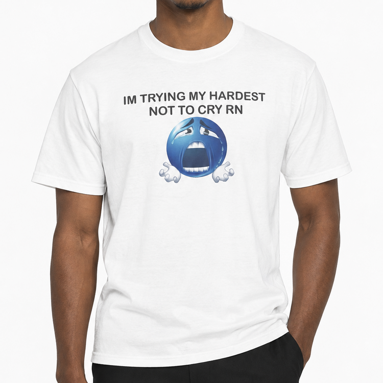 A man wearing a white short-sleeve graphic t-shirt with the text 'IM TRYING MY HARDEST NOT TO CRY RN' and a blue crying face emoji, paired with black pants, against a plain white background.